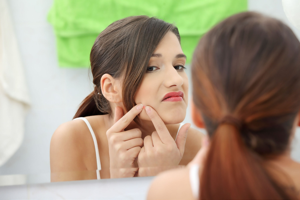 Woman looking at the mirror to get rid of her pimples